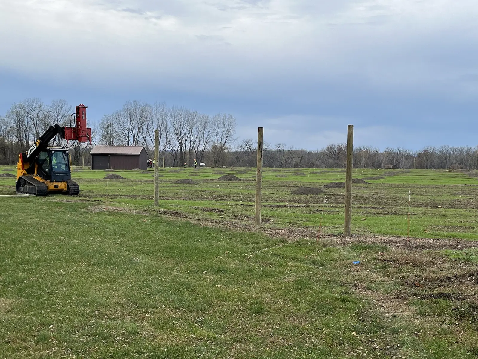 Tracked auger and wood posts set along a new fence line in an open field