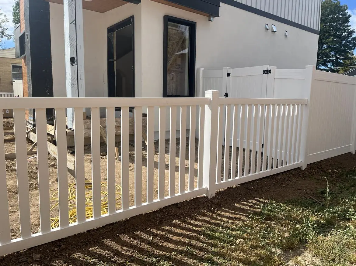 White vinyl fence and gate beside a house under construction
